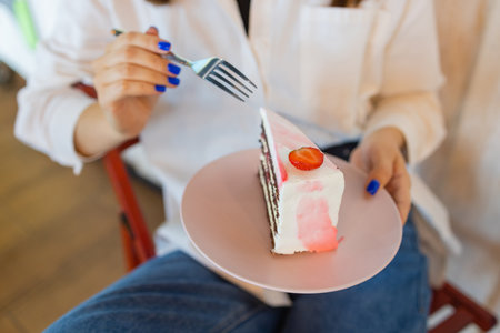 Young woman eating dessert in restaurant, close-up. Top view of females hands holding fork with piece of cherry pie next to plate with slice of cake.の写真素材