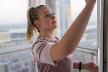 Beautiful young housewife in working clothes washing windows by professional tools at home.の写真素材
