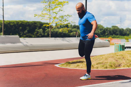 Young athlete running fast outdoors. Wearing sport cloth, doing wide step, demonstrating healthy way...