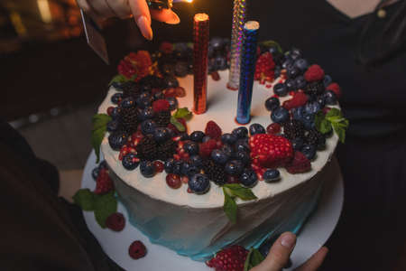 Birthday cake with candles. Candles on cake. Cake for holiday. Beautiful white cake with strawberries on dark background. Vertical photo.の写真素材