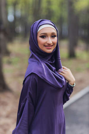 Islamic beautiful woman in a Muslim dress standing on a summer park street background forest autumn trees.world hijab day.の写真素材