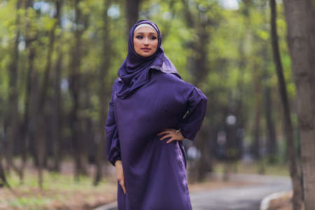 Islamic beautiful woman in a Muslim dress standing on a summer park street background forest autumn trees.world hijab day.の写真素材