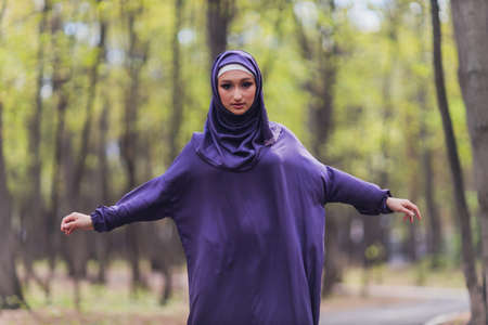 Islamic beautiful woman in a Muslim dress standing on a summer park street background forest autumn trees.world hijab day.の写真素材