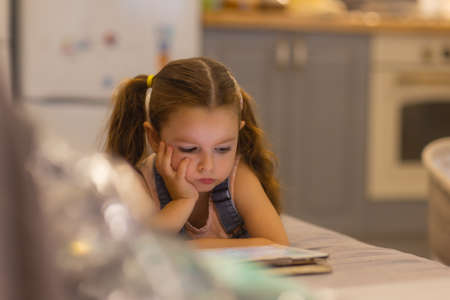 Smiling little girl lying on comfortable couch, enjoying playing online game on digital tablet...