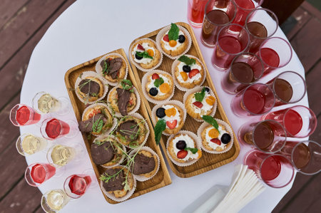 Elegant glasses with chilled champagne stand in row next to canapes and snacks on picturesque background. Party and holiday away. Picnic.の写真素材