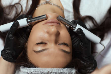 Cosmetology. Beautiful Woman At Spa Clinic Receiving Stimulating Electric Facial Treatment From...