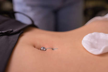 The first piercing. Dressing the earrings on the navel. Female piercing.の写真素材