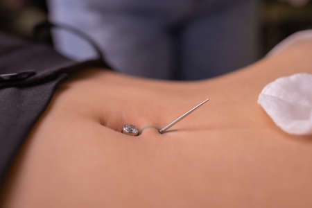 The first piercing. Dressing the earrings on the navel. Female piercing.の写真素材
