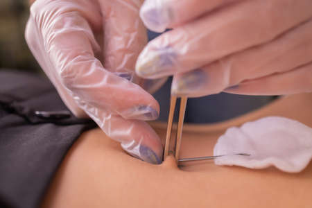 The first piercing. Dressing the earrings on the navel. Female piercing.の写真素材