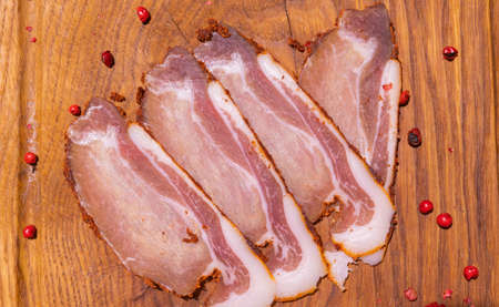 Sliced smoked gammon on a wooden table with addition of fresh herbs and aromatic spices.の写真素材