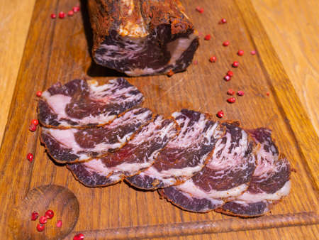 Sliced smoked gammon on a wooden table with addition of fresh herbs and aromatic spices.の写真素材