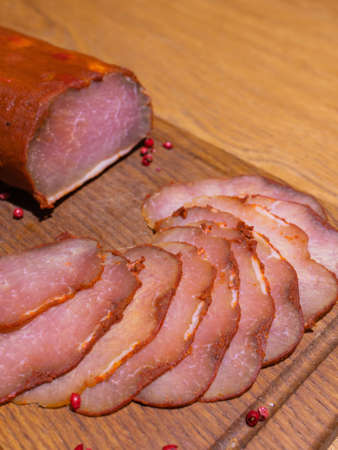 Sliced smoked gammon on a wooden table with addition of fresh herbs and aromatic spices.の写真素材