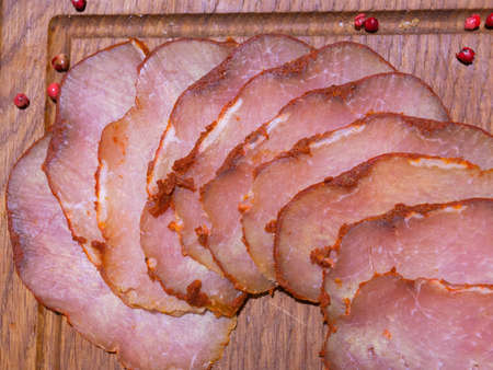 Sliced smoked gammon on a wooden table with addition of fresh herbs and aromatic spices.の写真素材