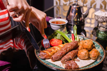 Woman eating barbecue in a cafe. Female hands close-up holding a fork with a piece of barbecue.