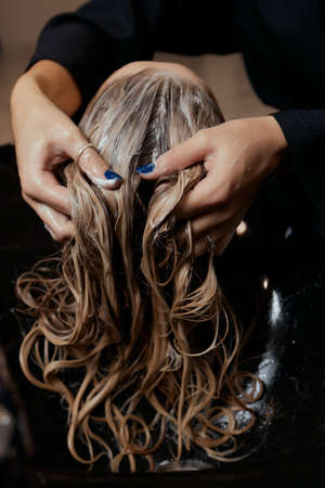 Hairdresser in beauty salon washes his client hair, before procedure of applying natural restoring ingredients and vitamins to hair and haircut.の写真素材