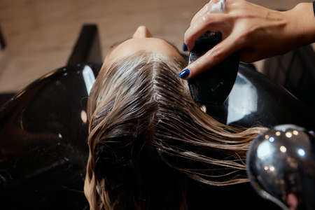 Hairdresser in beauty salon washes his client hair, before procedure of applying natural restoring ingredients and vitamins to hair and haircut.の写真素材
