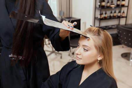 Hair stylist makes bouffant using comb on thin strands. Shatush technique for hair lightening.