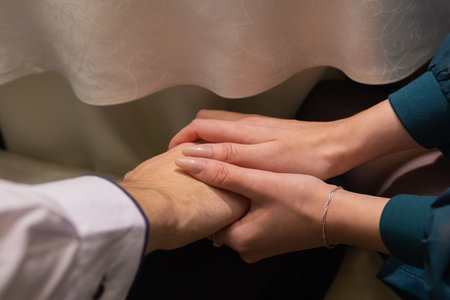 Cropped shot of young couple holding hands while sitting together. Focus on hands.の写真素材
