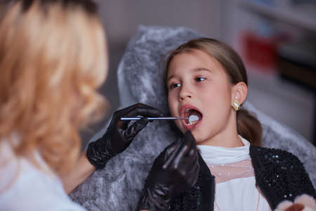 Caucasian young child girl sitting in medical chair while dentist fixing teeth at dental clinic...
