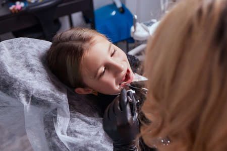 Caucasian young child girl sitting in medical chair while dentist fixing teeth at dental clinic using dental tools instruments, close-up photo of face. professional medical specialist.の写真素材