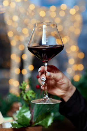 Female hand holding a glass of champagne against the background of a christmas tree, celebrating christmas alone concept, close-up.の写真素材
