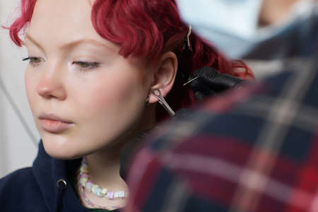 A beautician makes a puncture of the earlobe with a disposable device in a beauty salon. Ear...