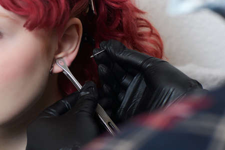A beautician makes a puncture of the earlobe with a disposable device in a beauty salon. Ear piercing lobe.の写真素材