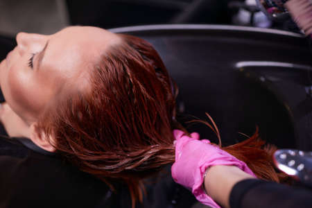 Hairdresser in beauty salon washes his client hair, before procedure of applying natural restoring ingredients and vitamins to hair and haircut.の写真素材