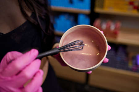 girl in white rubber protective gloves holding a brush in her hands and stirring hair dye close-up colorist hair care at home hair mask.の写真素材