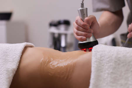procedure removing cellulite on female abdomen, cavitation belly massage. Ultrasonic massage for weight loss. Correction of female figure without surgical intervention. Closeup of the tummy.の写真素材