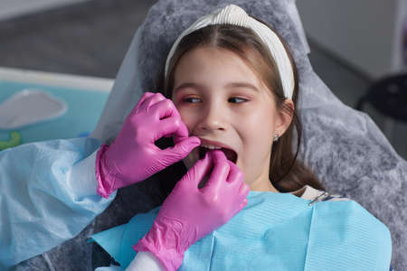 Cut view hands in latex gloves to floss child front teeth. Woman hold dental tools beside.の写真素材