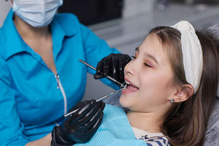 The dentist examines the baby girls baby teeth, the treatment of baby teeth, the dentist holds a mirror in his hands, caries in a child.の写真素材