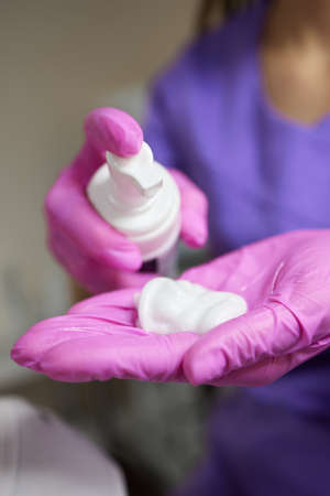 Close-up, a woman in a white robe presses on the dispenser of beauty care products, blurred...