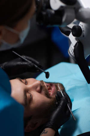 The dentist treats his patients teeth with a microscope. The dentist treats the patients mouth....