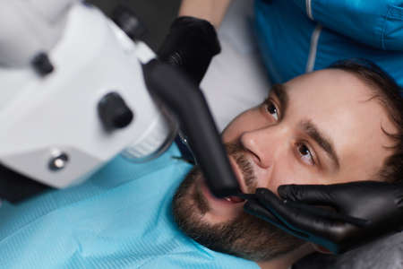 The dentist treats his patients teeth with a microscope. The dentist treats the patients mouth. Dental care.の写真素材
