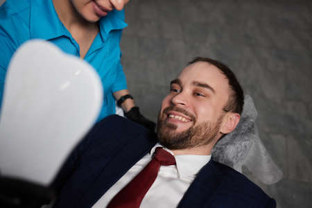 Smiling young man sitting in dentist chair while doctor examining his teeth.の写真素材