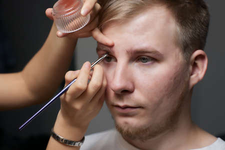 Professional barber doing threading procedure and correcting shape of eyebrows to young male client...