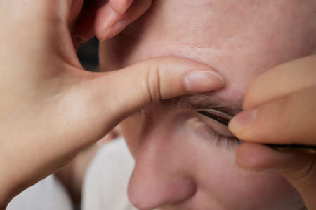 Professional barber doing threading procedure and correcting shape of eyebrows to young male client...