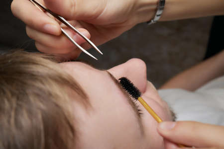 Professional barber doing threading procedure and correcting shape of eyebrows to young male client...