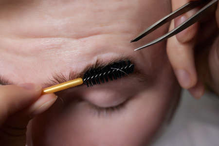 Professional barber doing threading procedure and correcting shape of eyebrows to young male client with tweezer in barber shop. Barber at work. Brow care concept. Plucking brows.の写真素材