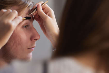 Professional barber doing threading procedure and correcting shape of eyebrows to young male client...