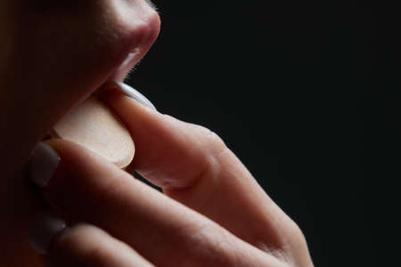 Close up of face of young woman taking drug. The drug addict is standing and putting a pill into her mouth.の写真素材