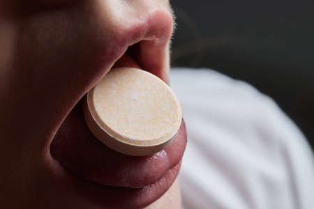 Close up of face of young woman taking drug. The drug addict is standing and putting a pill into her mouth.の写真素材