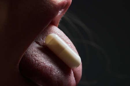 Close up of face of young woman taking drug. The drug addict is standing and putting a pill into her...