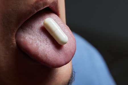 Man taking pill, mouth open with tongue sticking out.