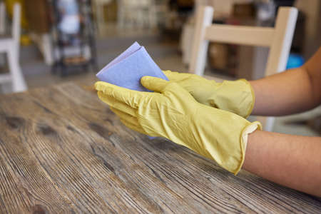 A mans hand in medical glove wipes the table with napkin. Background waiter in an apron in blur. Surface treatment.の写真素材