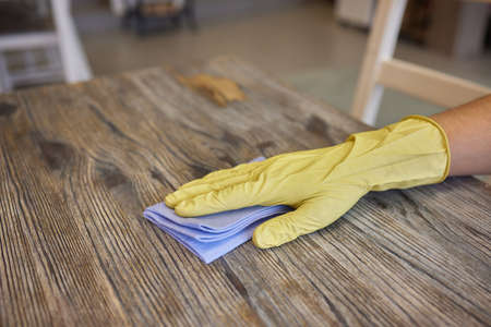 A mans hand in medical glove wipes the table with napkin. Background waiter in an apron in blur....
