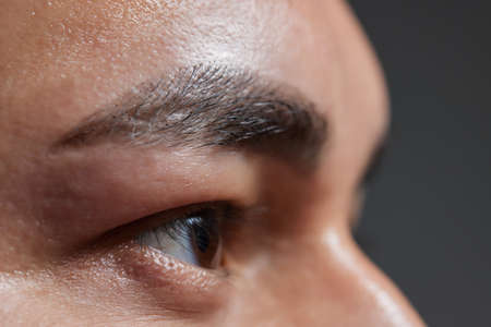 Professional barber doing threading procedure and correcting shape of eyebrows to young male client with tweezer in barber shop. Barber at work. Brow care concept. Plucking brows.の写真素材