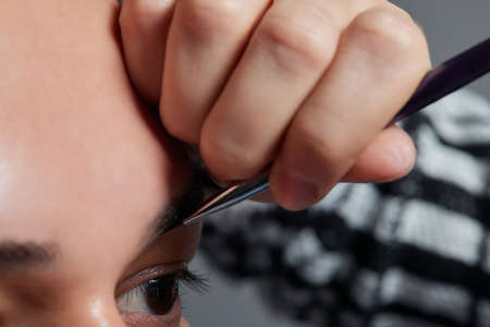 Professional barber doing threading procedure and correcting shape of eyebrows to young male client...
