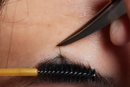 Professional barber doing threading procedure and correcting shape of eyebrows to young male client...